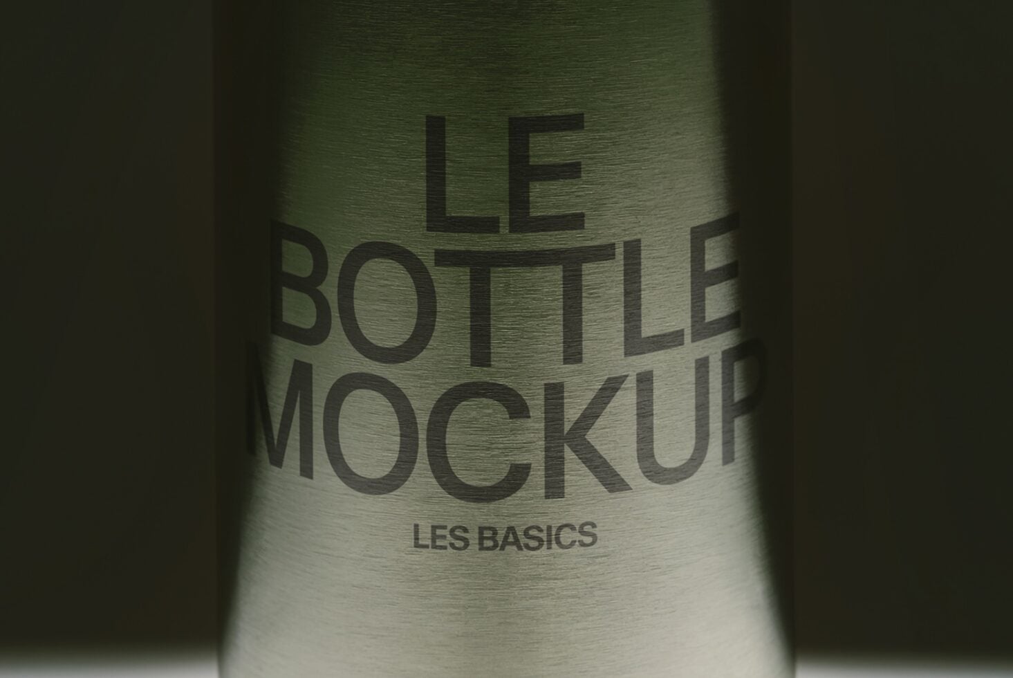 Glass bottle with embossed text reading "LE BOTTLE MOCKUP LES BASICS" on brushed metallic surface
