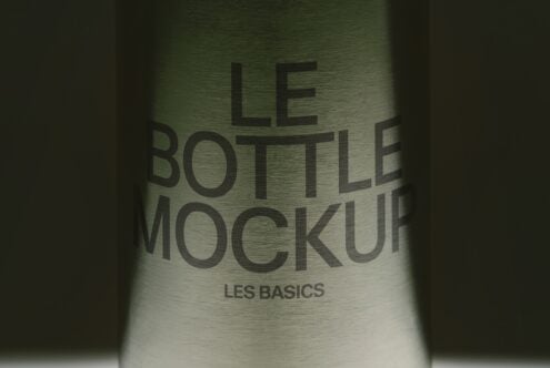 Glass bottle with embossed text reading "LE BOTTLE MOCKUP LES BASICS" on brushed metallic surface