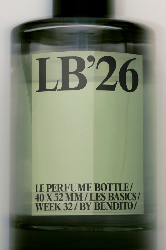 Dark glass perfume bottle mockup with cream label showing LB'26 branding