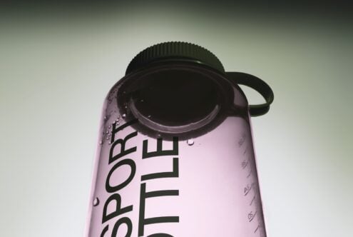 Pink water bottle with black cap, condensation droplets, minimal gradient background