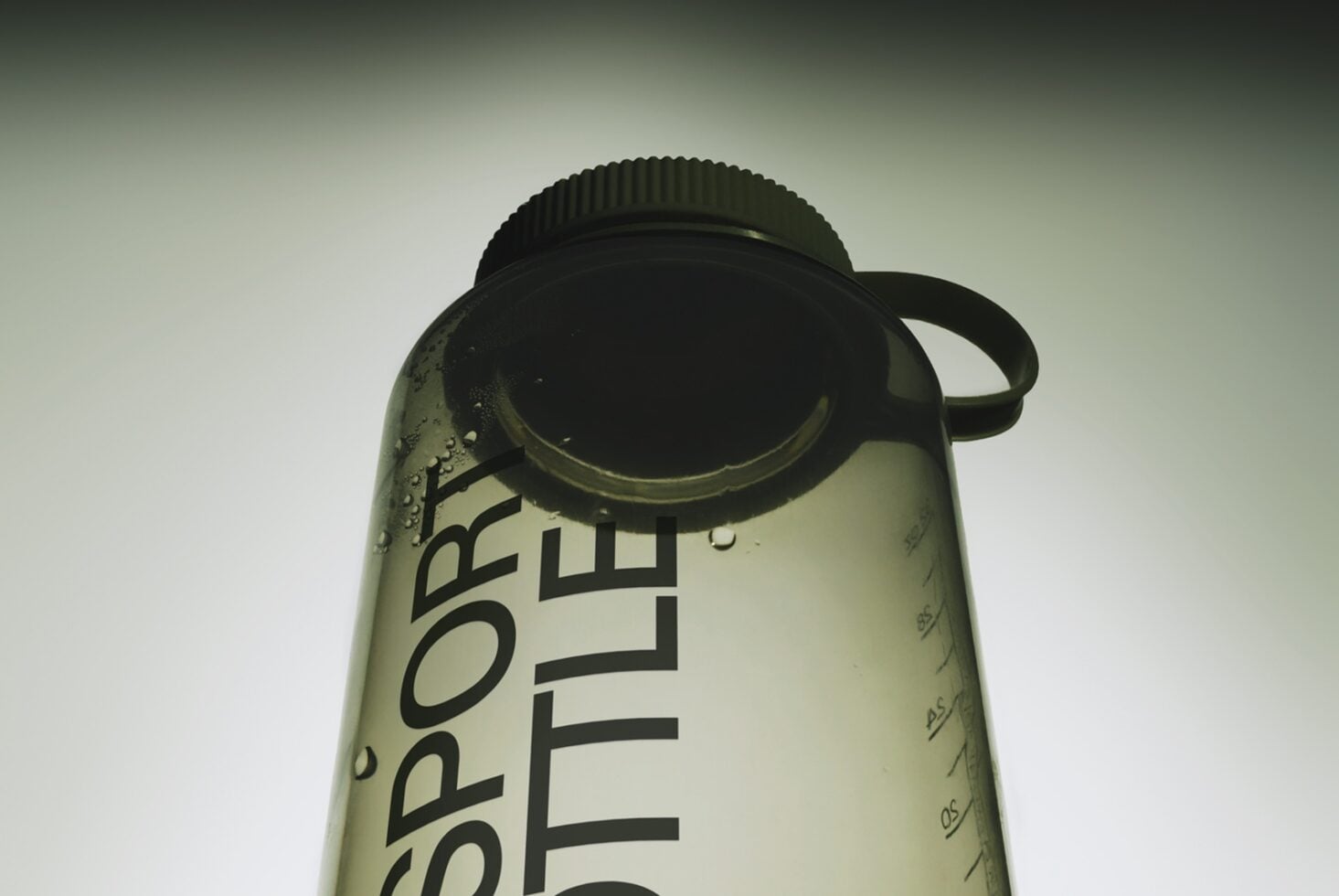 Water bottle mockup with condensation droplets, black cap, visible label, shot from above on soft gradient background