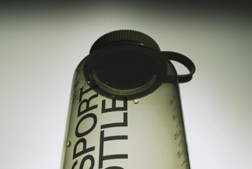 Water bottle mockup with condensation droplets, black cap, visible label, shot from above on soft gradient background