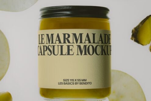 Glass jar with green metal lid filled with yellow marmalade, cream label, lemon slices scattered around
