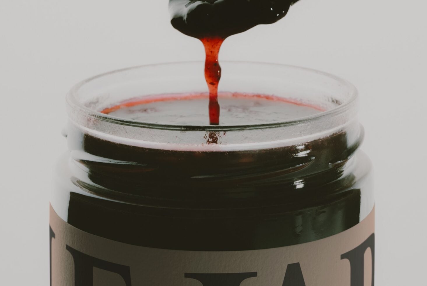 Red liquid dripping from brush into glass jar filled with dark paint or ink mixture