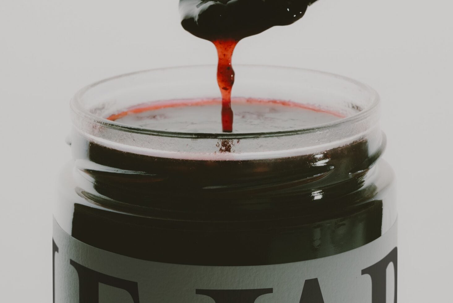 Red liquid dripping from brush into glass jar with dark paint swatches stacked inside