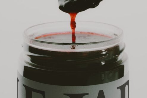 Red liquid dripping from brush into glass jar with dark paint swatches stacked inside