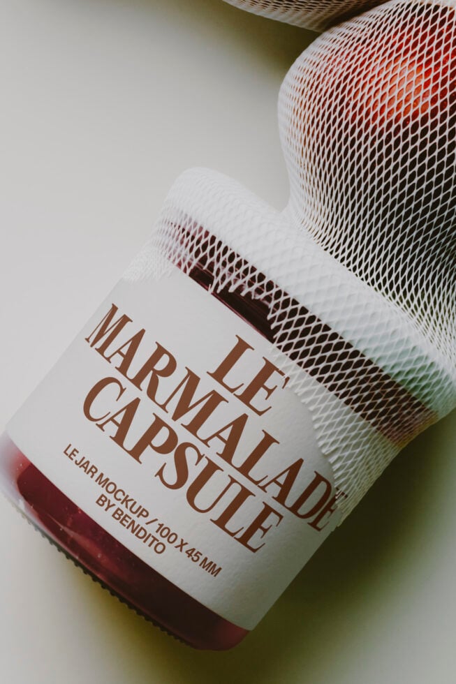Overhead shot of red liquid in glass jar with mesh wrap, brown label reading "Le Marmalade Capsule"