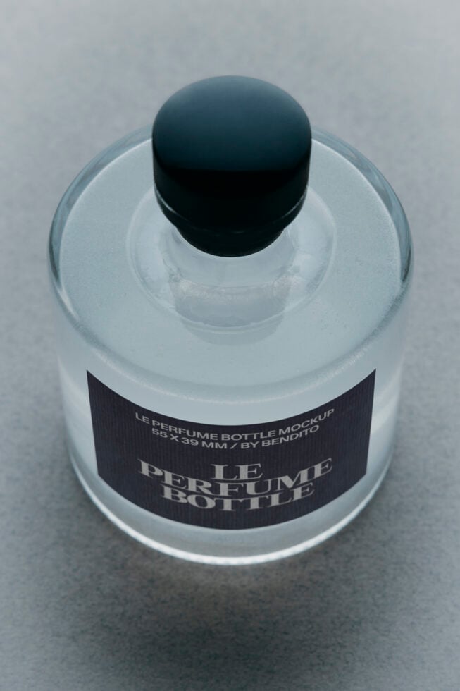 Overhead shot of frosted glass perfume bottle with black cap, black label mockup on gray surface