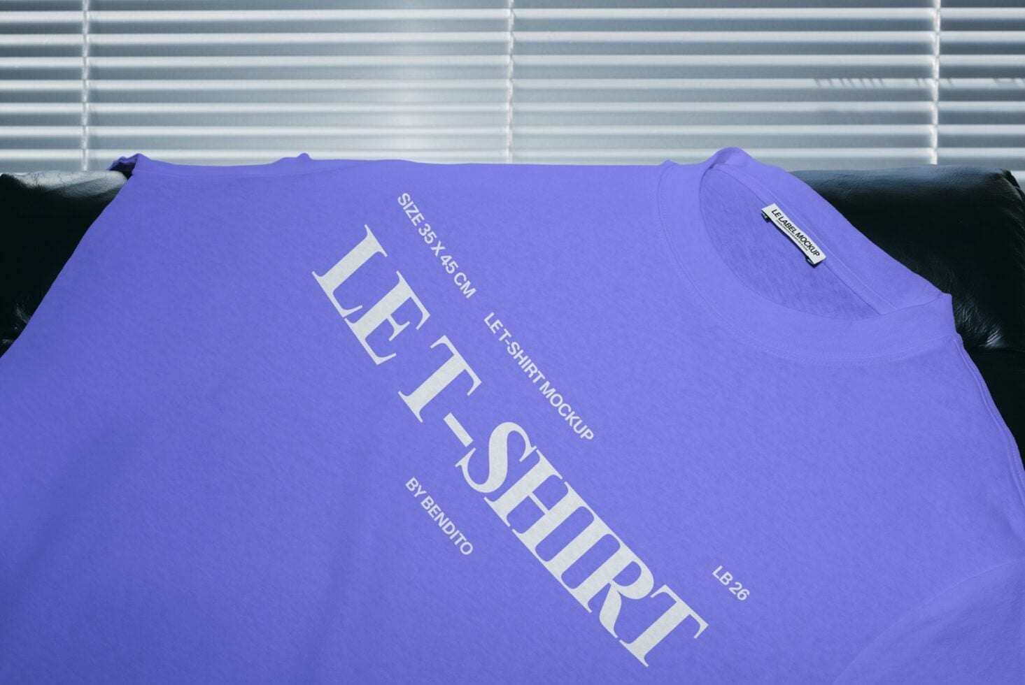 Bright purple tee draped on black couch with white graphic text print against venetian blinds background