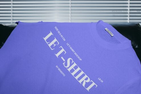 Bright purple tee draped on black couch with white graphic text print against venetian blinds background