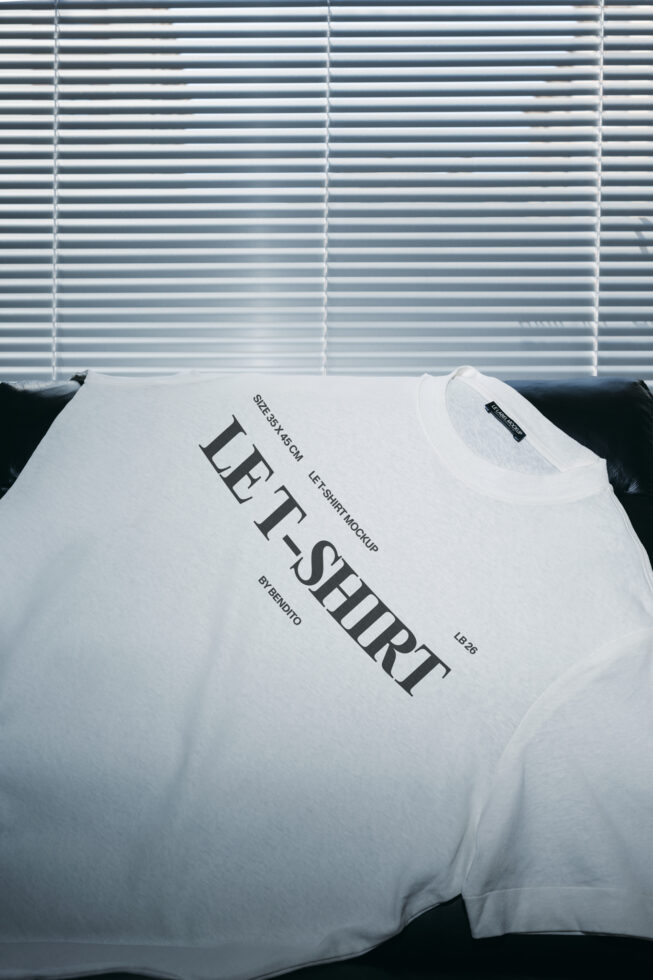 White tee on black couch with diagonal text print, venetian blinds in background