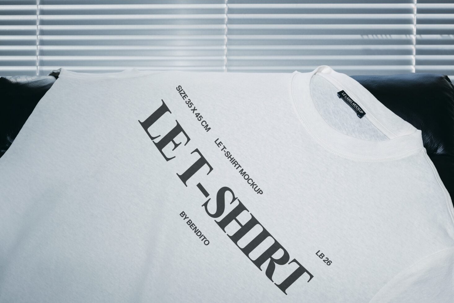 White crewneck tee draped on black couch with size specs, clean minimal design mockup