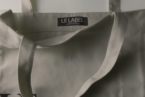 Beige canvas tote bag with black woven label showing "LE LABEL" branding