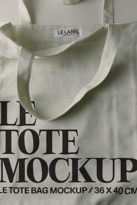 Cream canvas tote bag with woven handles, flat lay showing label close-up