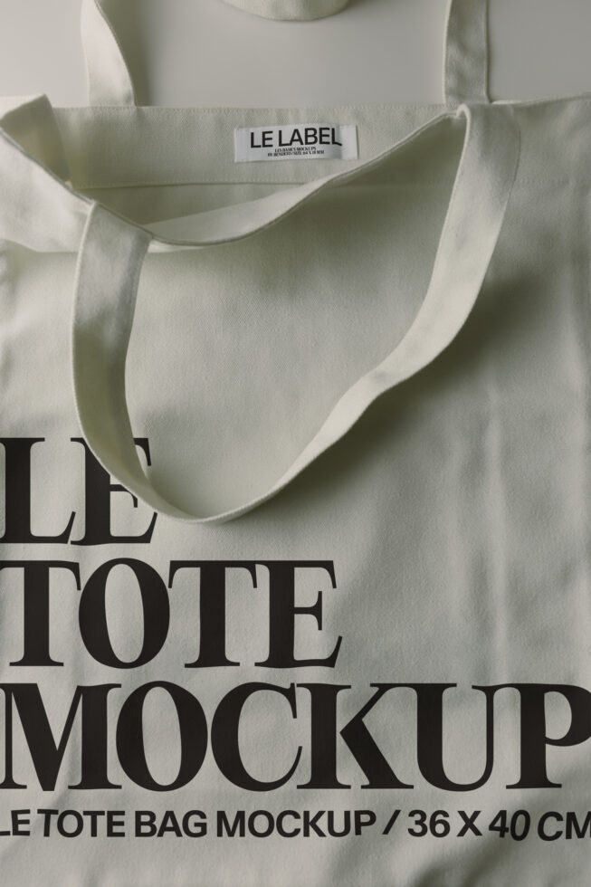 Cream canvas tote bag with woven handles, flat lay showing label close-up