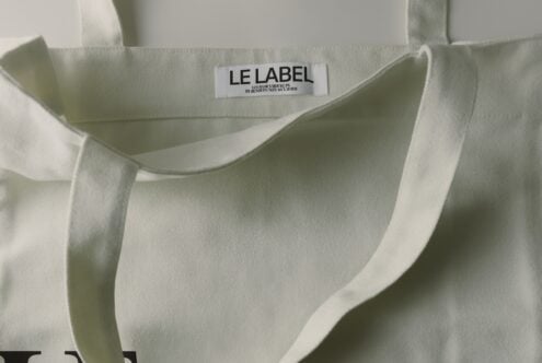 Cream tote bag with woven label mockup showing care instructions text on natural fabric