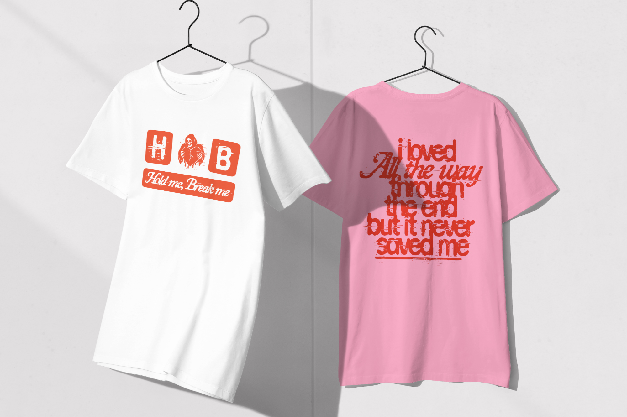 Two tees on hangers, white with red graphic, pink with red script text on back