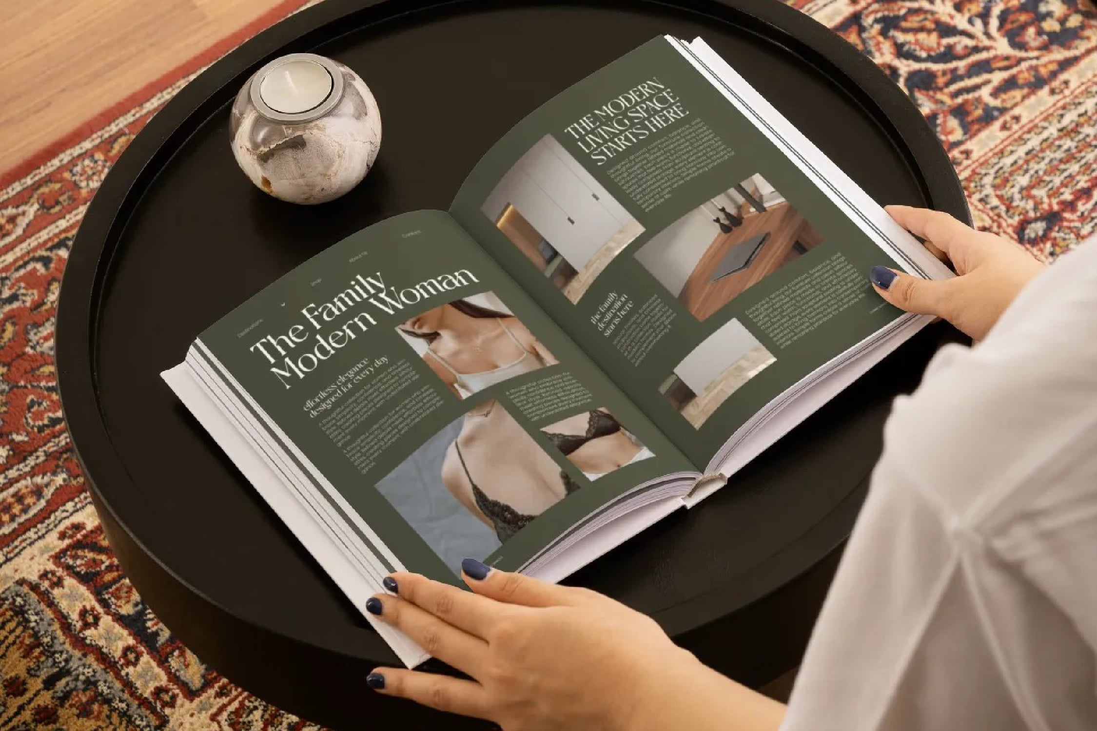 Open magazine spread with sage green pages showing fashion photography, hands holding it on black tray with decorative rug
