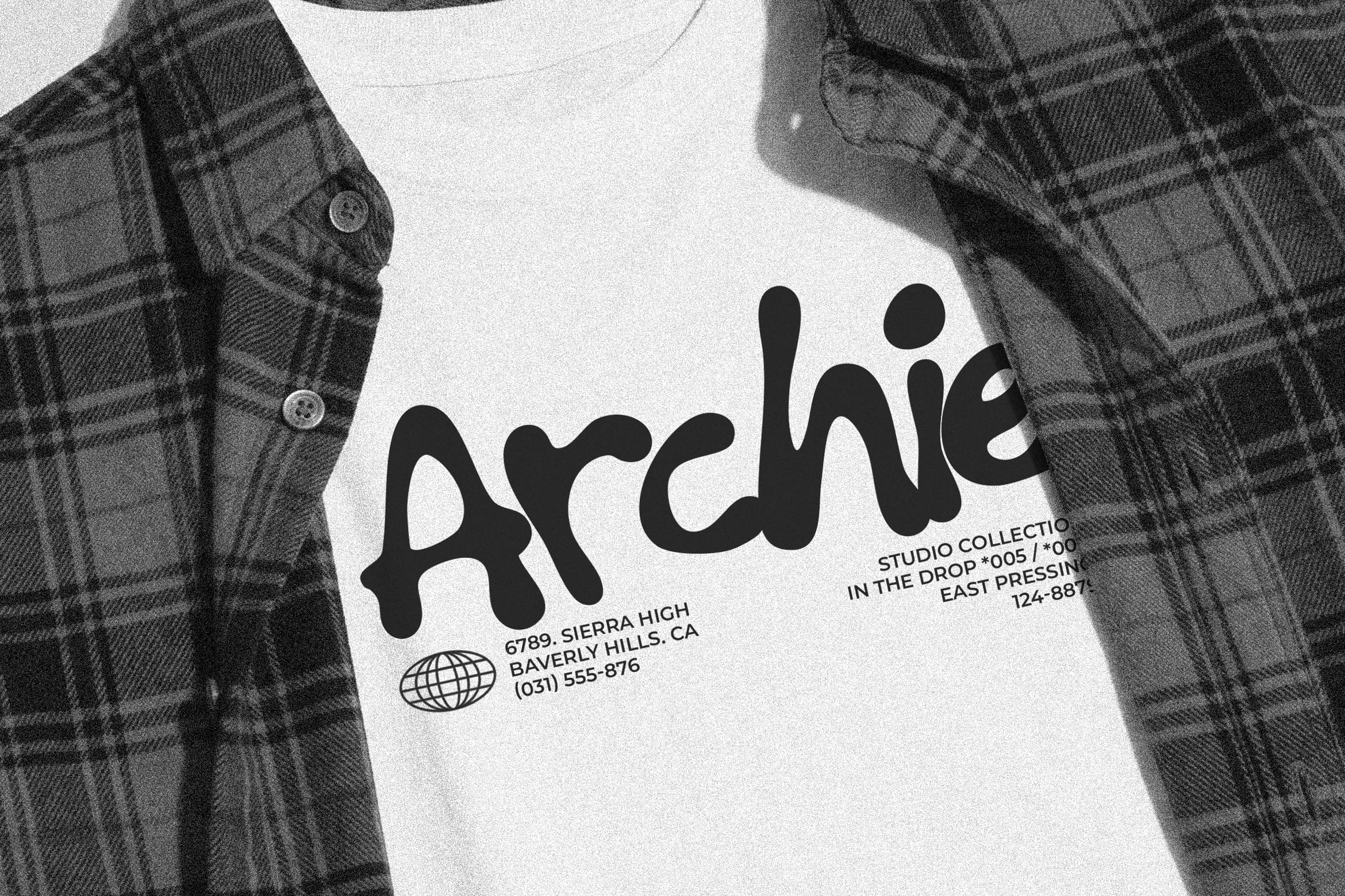 White tee with bold "Archie" typography, studio details, worn with plaid shirt jacket
