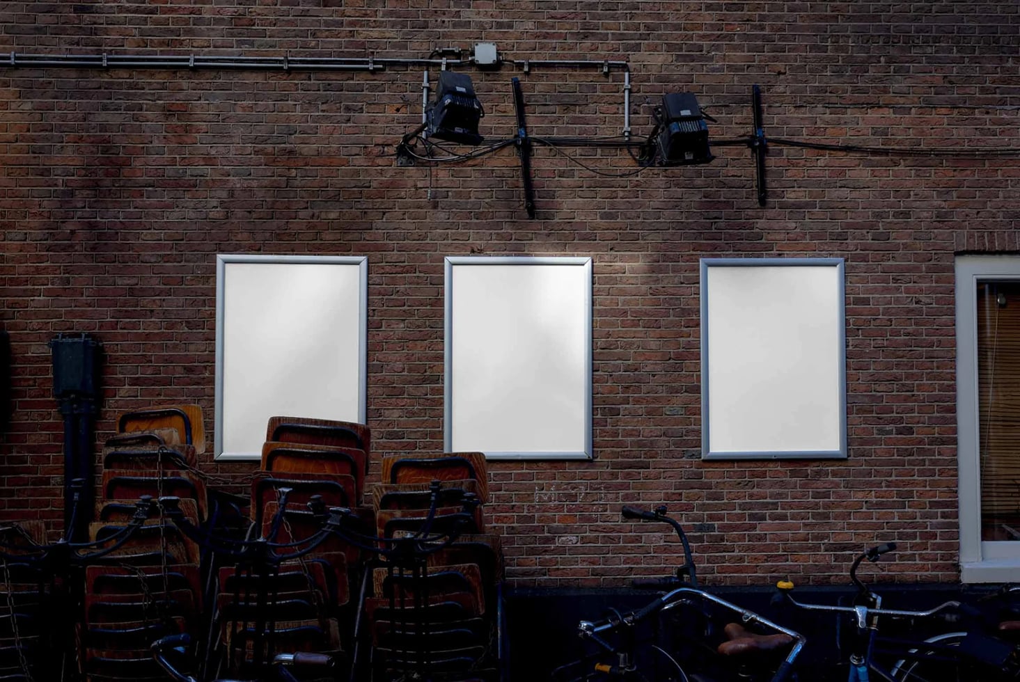 Industrial brick wall with three framed posters, studio lights, stacked chairs, bikes below