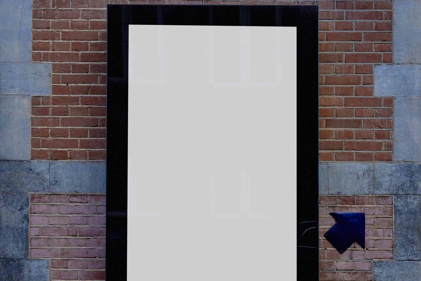 Blank poster mockup on brick wall with black frame, blue arrow pointing right