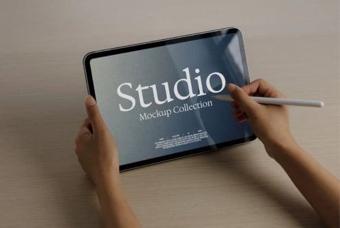 Hands holding tablet with stylus showing Studio Mockup Collection title on blue screen