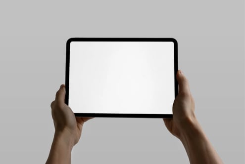 Hands holding tablet horizontally with blank white screen against gray background