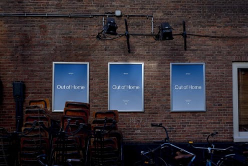 Street-facing brick wall with three illuminated poster mockups displaying "Out of Home" campaign