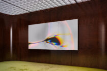 Large gallery display screen showing vibrant rainbow light refraction with flowing lines on dark wood walls
