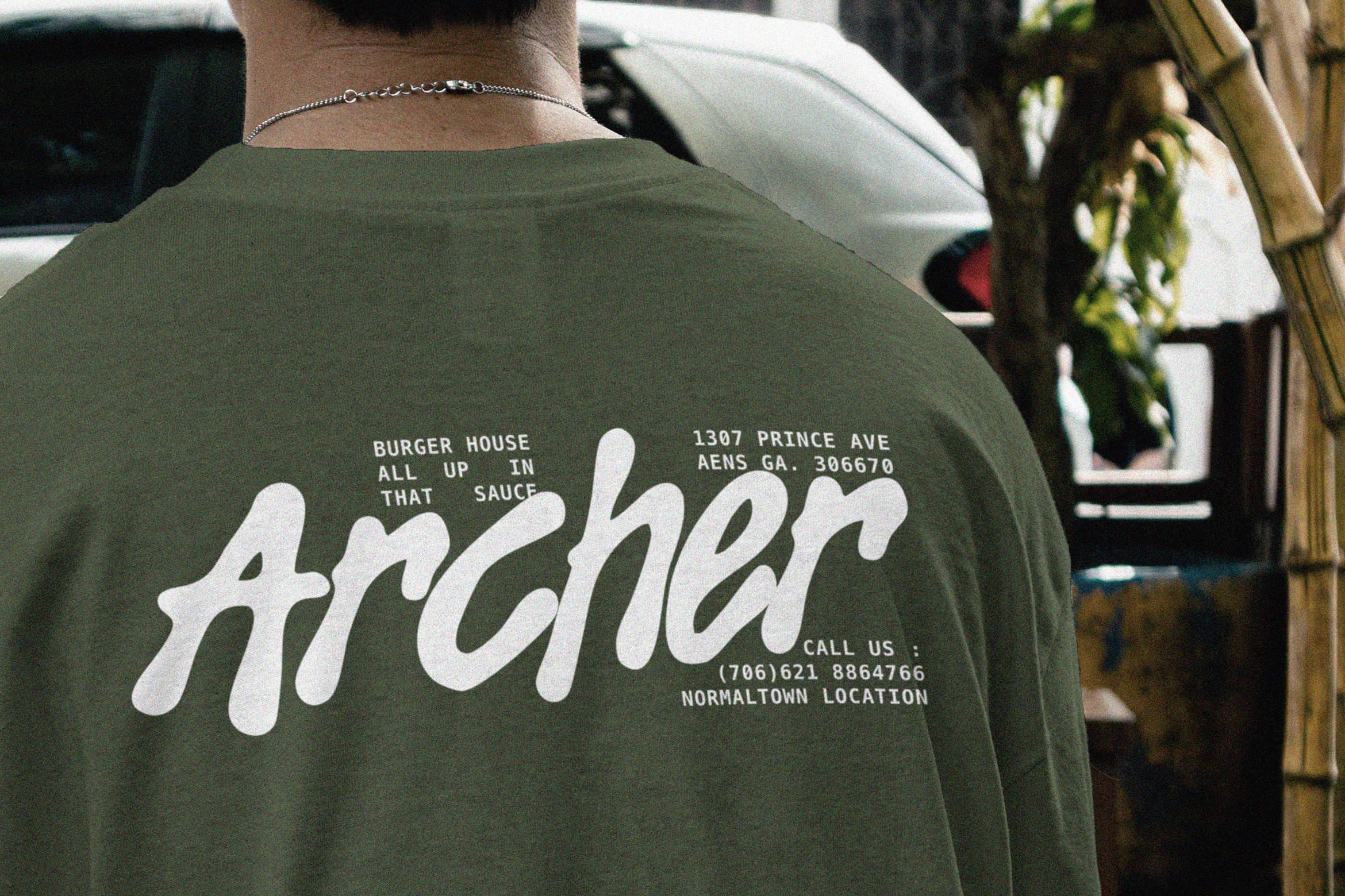 Olive tee with retro burger house branding on back, silver chain necklace visible