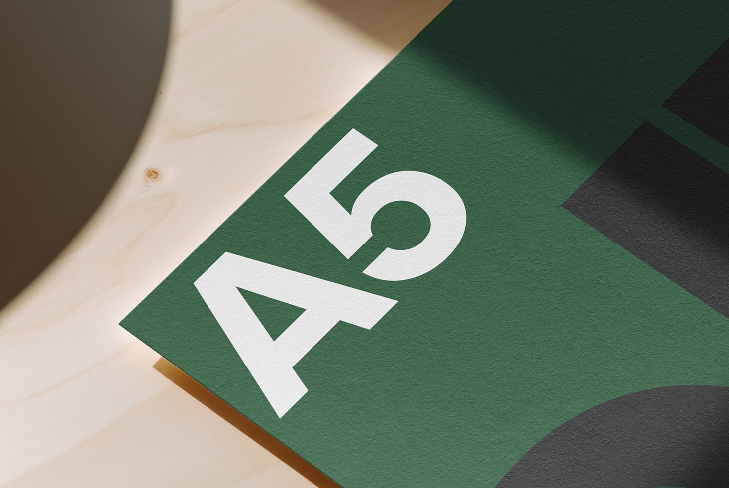 White geometric logo on green paper with natural wood surface, angled overhead shot