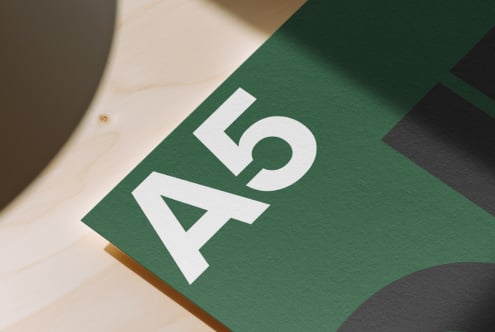 White geometric logo on green paper with natural wood surface, angled overhead shot