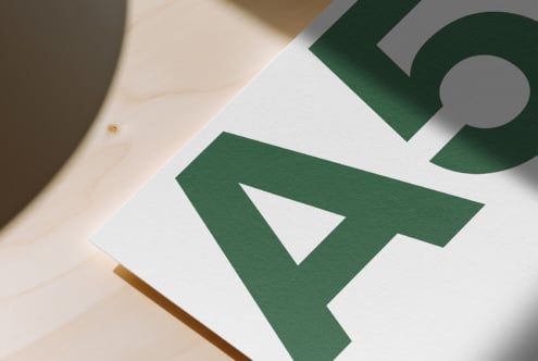 White paper with green geometric shapes on natural wood surface with soft shadows