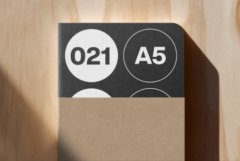 A5 notebook mockup with dark cover showing circular badge design on wooden surface