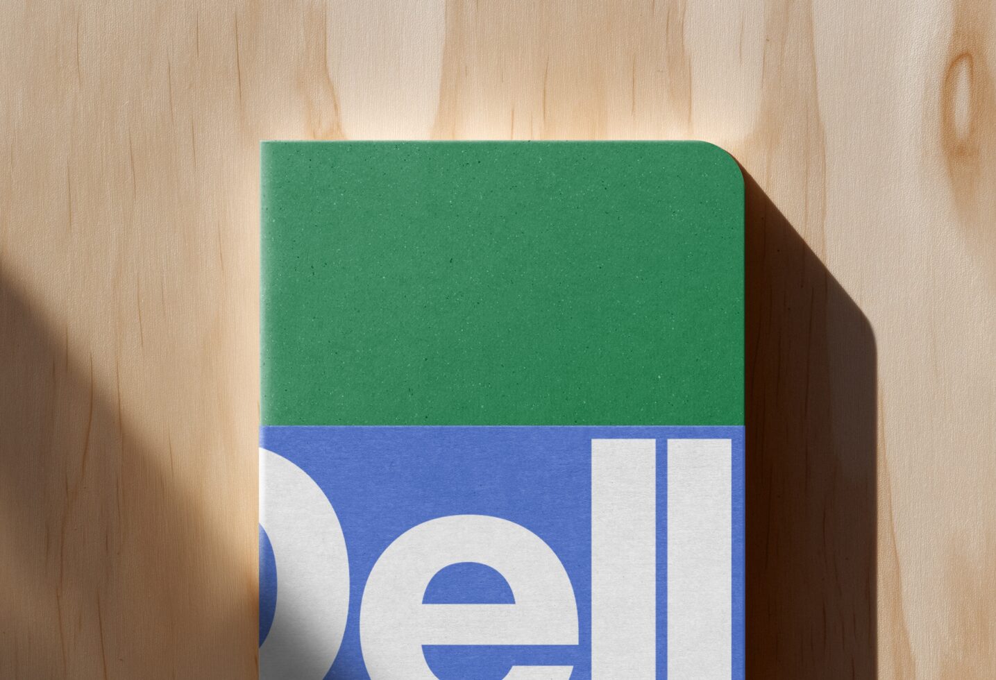 Rounded green box with blue stripe below showing partial white letterforms on natural wood background