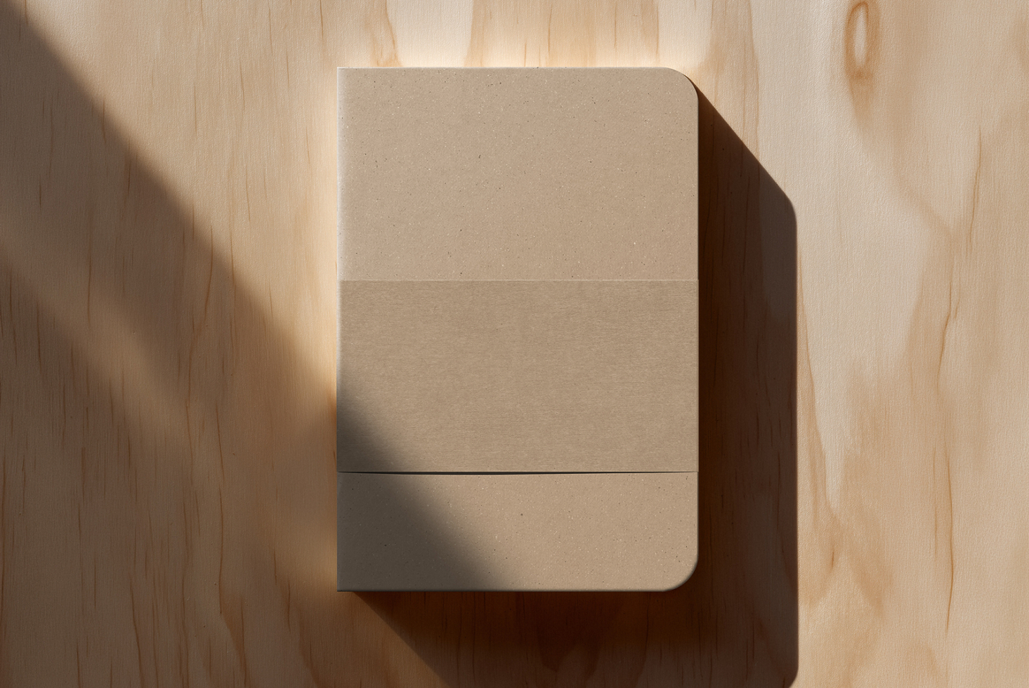 Beige notebook with rounded corners casting sharp shadow on light wood surface