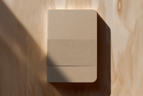 Beige notebook with rounded corners casting sharp shadow on light wood surface