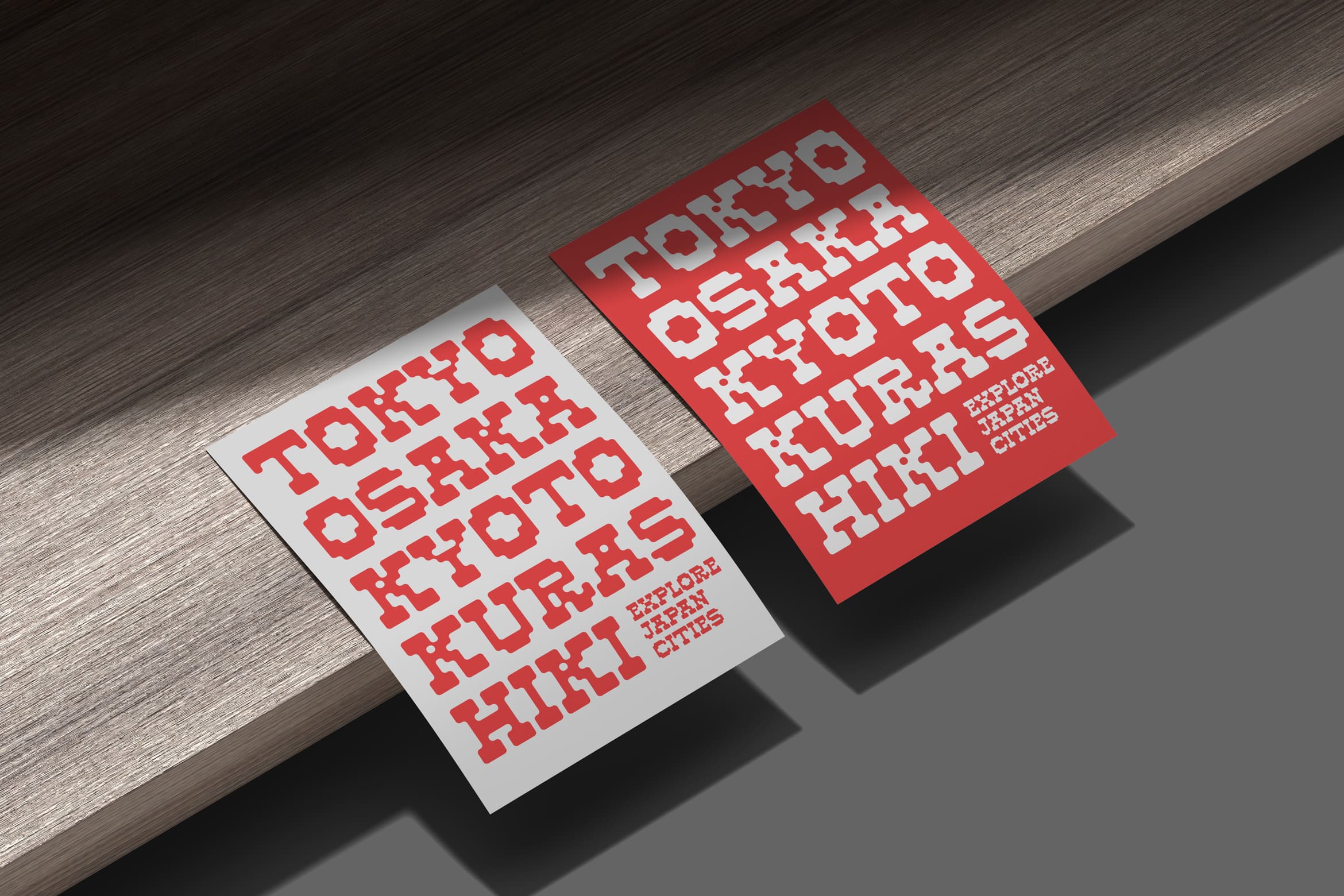 Two stacked postcards with bold red pixelated type on white or red stock, casting shadows on wood surface