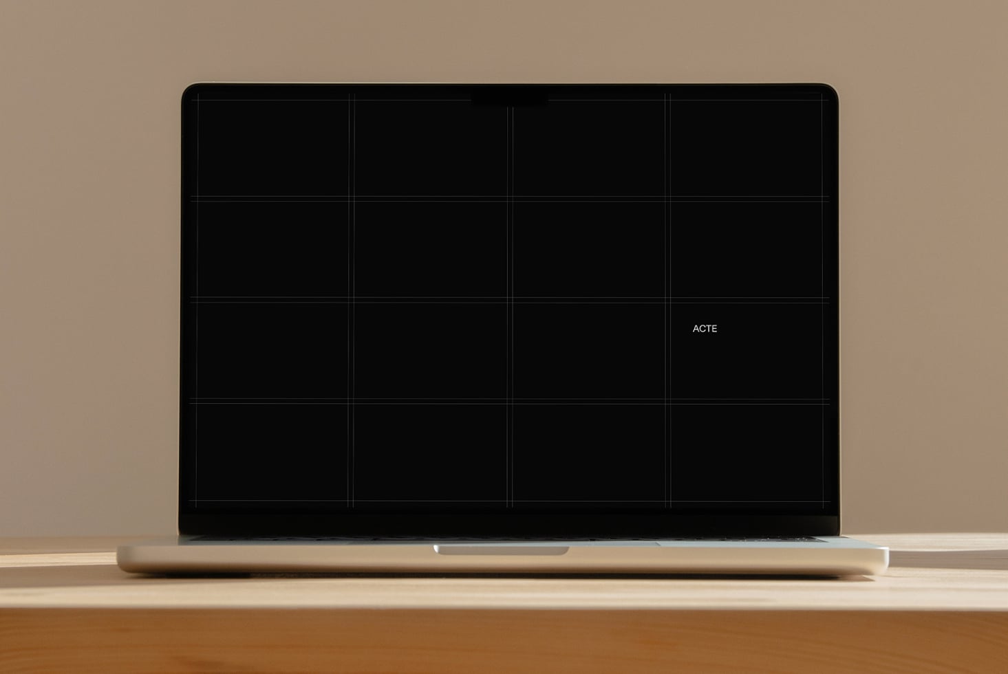 Laptop mockup with 16-panel grid layout on black screen, minimal branding on tan desk