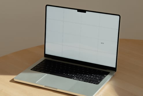 Laptop mockup on wood desk with gridded screen showing editable layout space