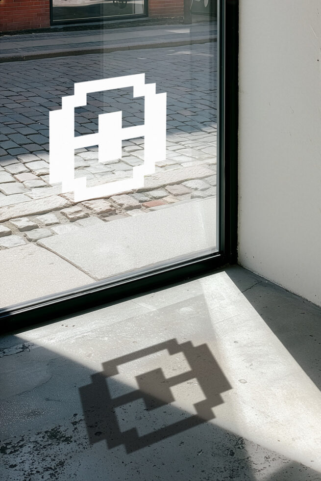 White geometric logo on storefront window with shadow cast on ground below