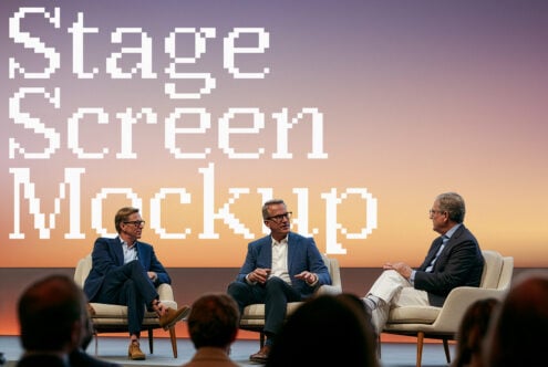 Three guys in blazers chatting on stage with pixelated retro text backdrop during conference panel discussion
