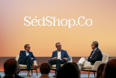 Three guys in blazers having a panel discussion on stage with warm gradient backdrop