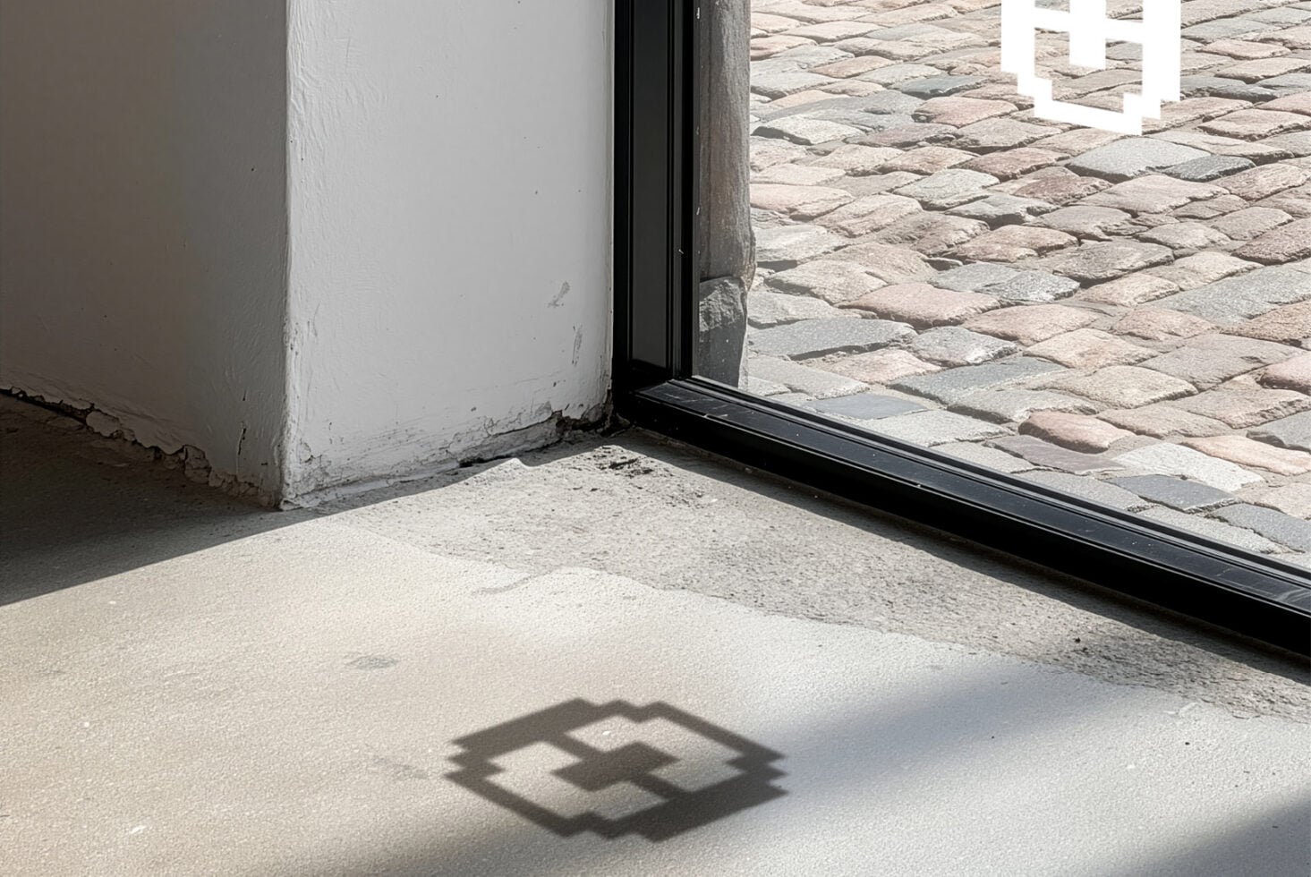Open doorway with black frame casting geometric shadow on concrete floor, whitewashed wall visible