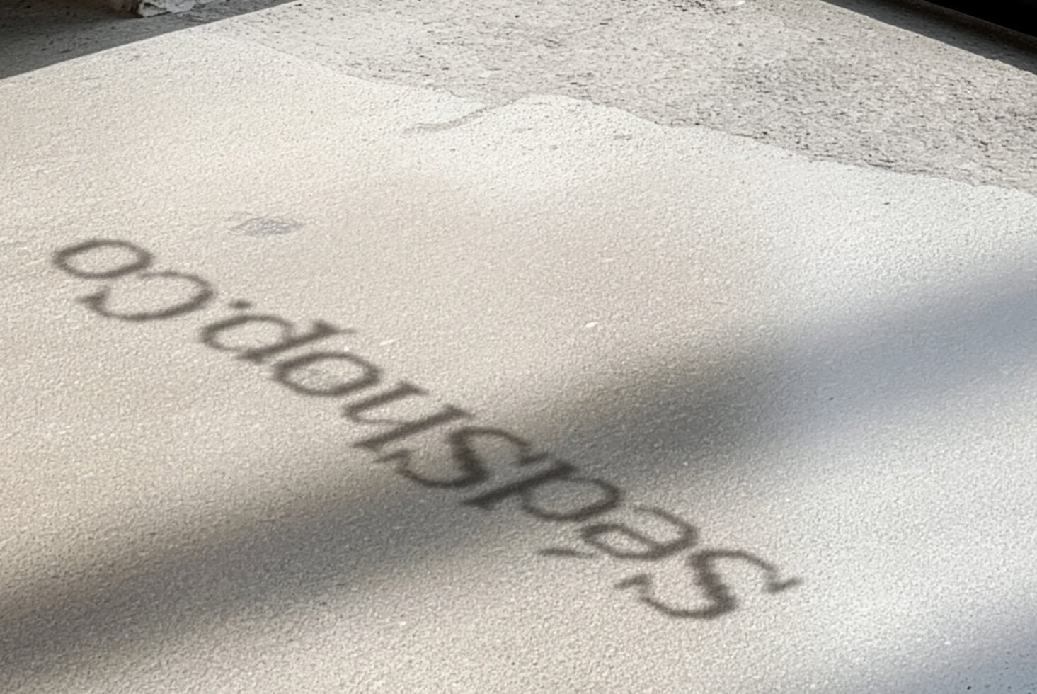 Embossed logo casting sharp shadow on concrete surface with natural sunlight
