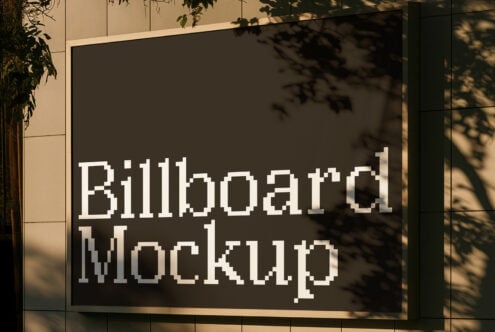 Outdoor billboard with pixelated white text on dark background, leaf shadows cast across