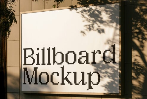 Billboard mockup with leaf shadows cast over cream background, black pixelated text, outdoor storefront setting