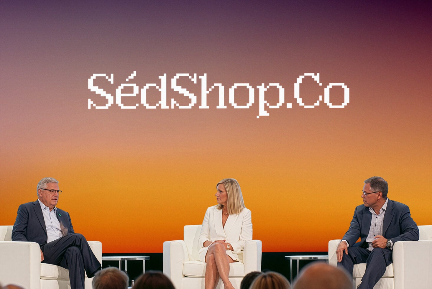Three professionals seated on stage with SedShop.Co pixelated text on gradient backdrop