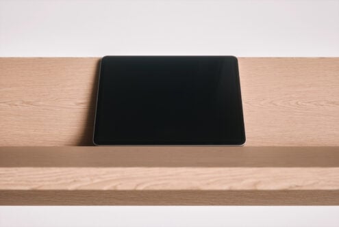 Tablet with blank screen sitting on light wood desk against white wall