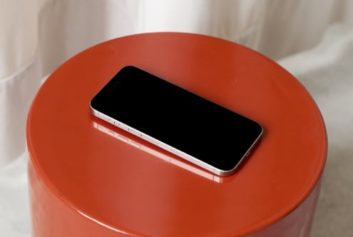 Smartphone with silver frame sitting on bright red circular platform, soft fabric backdrop